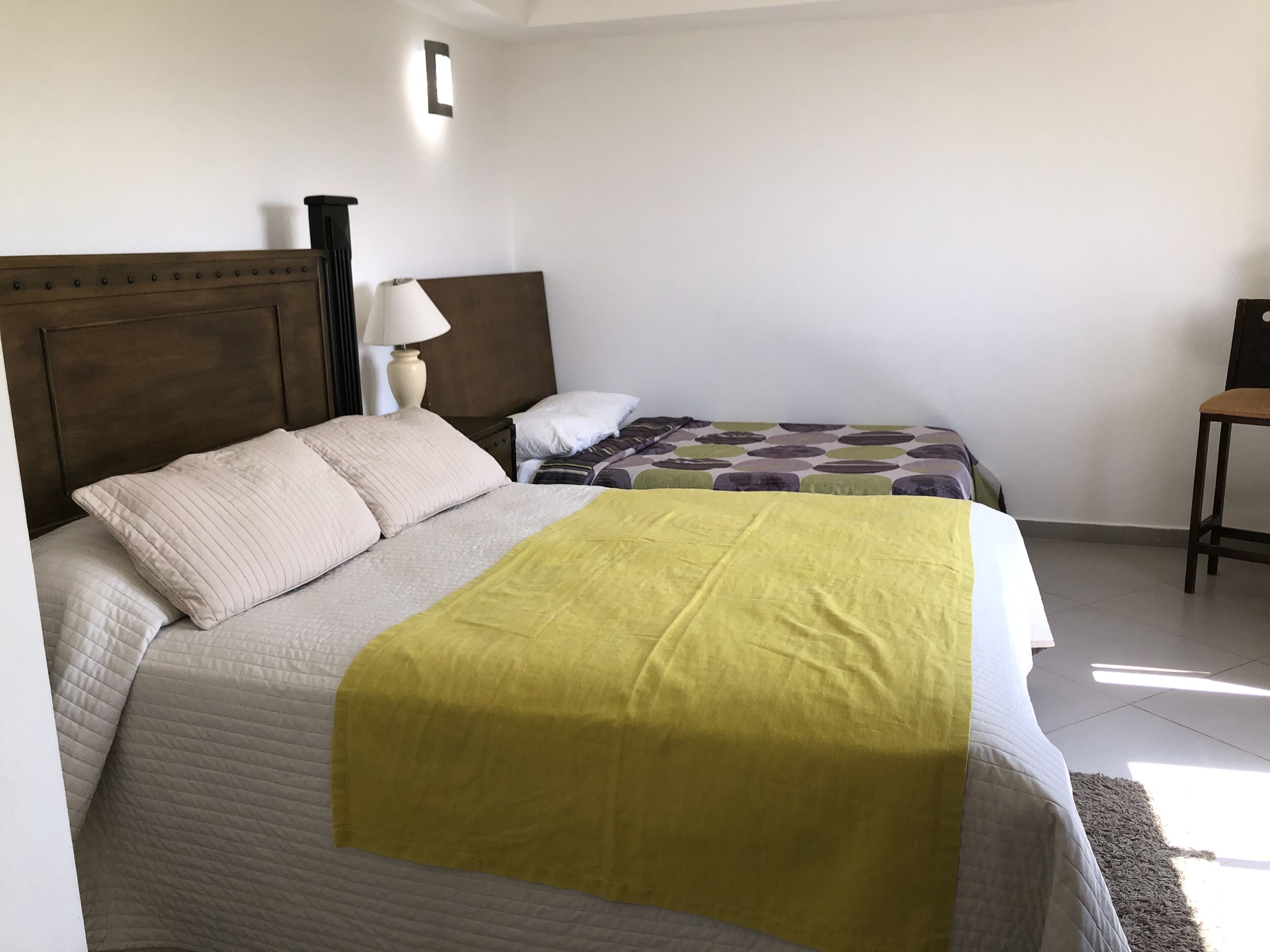 Ein Schlafzimmer mit zwei Betten, einem Nachttisch, einer Lampe und einem Sessel.