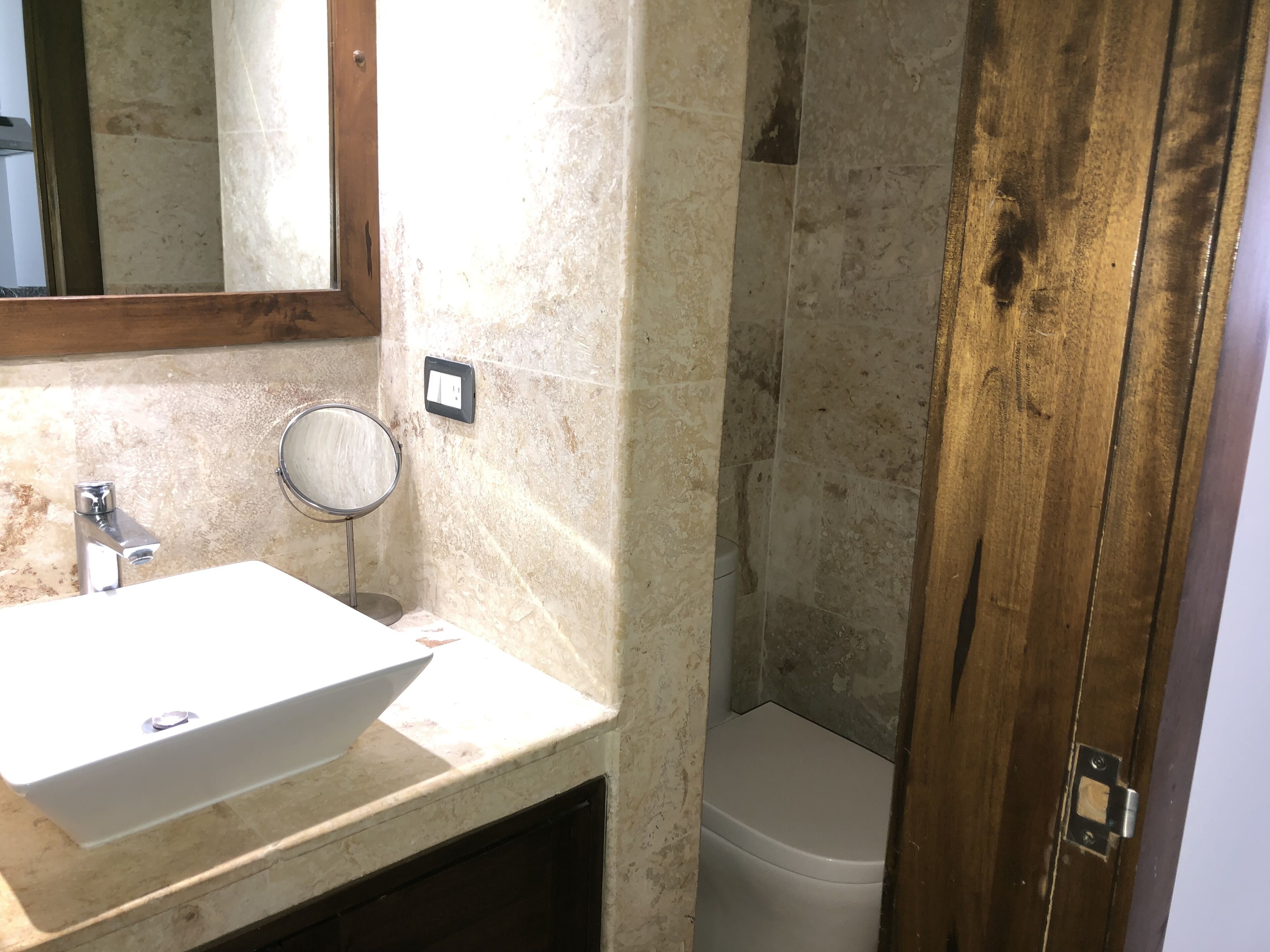 Un baño con un lavamanos blanco, un espejo redondo y un inodoro.