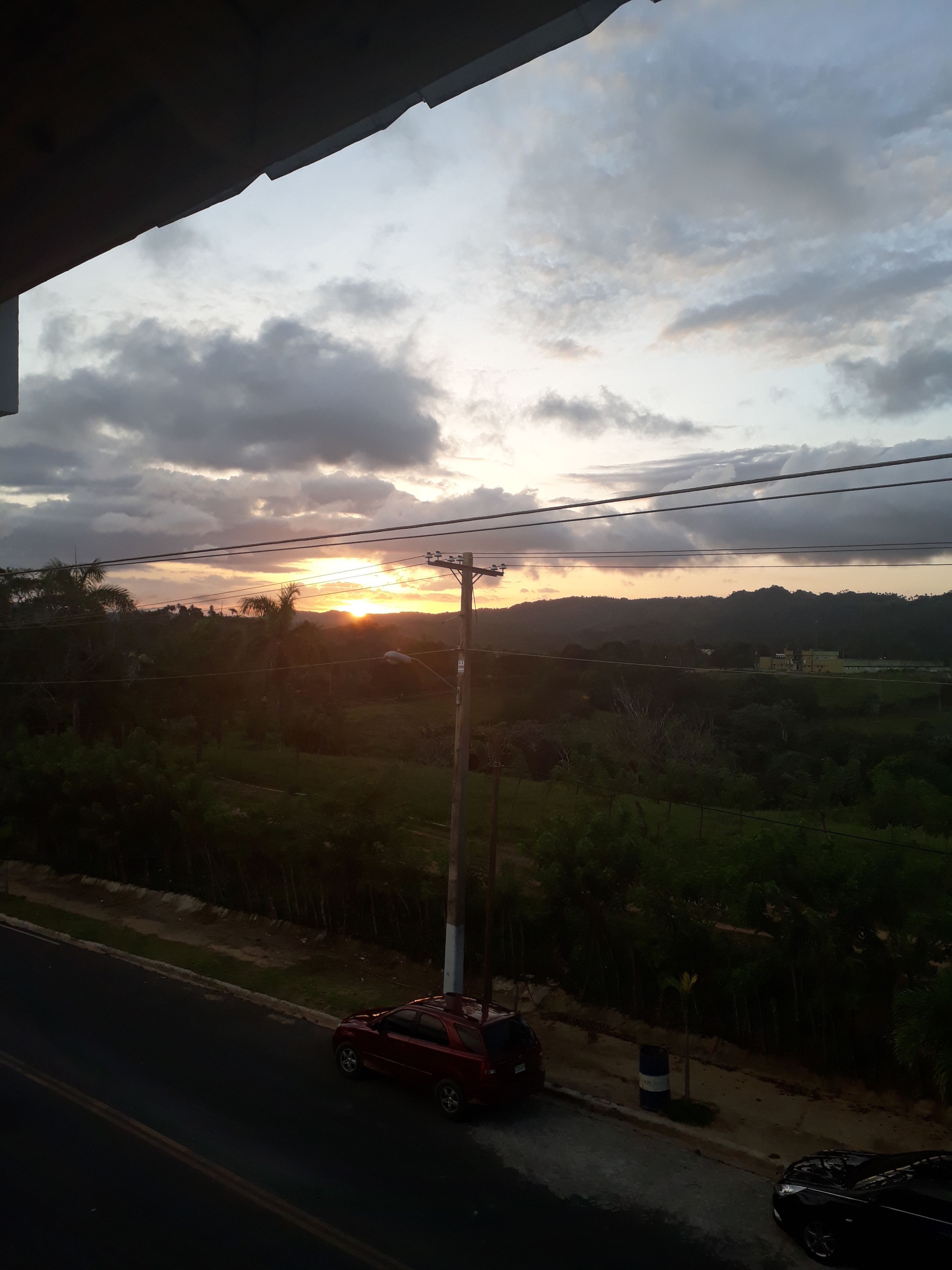 A sunset with clouds, a road, and a car.