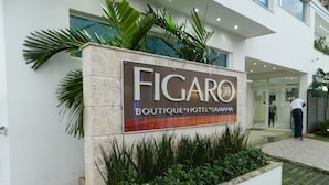 A sign for Figaro Boutique Hotel & Samana, featuring a modern building facade with a landscaped area in front. - Figaro Hotel Boutique (Samaná)