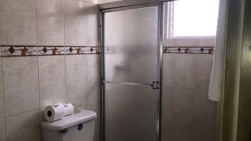 Une salle de bain comprenant des toilettes, une douche à parois de verre et une fenêtre.