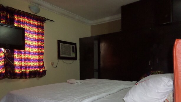Een hotelkamer met een bed, een aan de muur bevestigde televisie en een raam met gordijnen.
