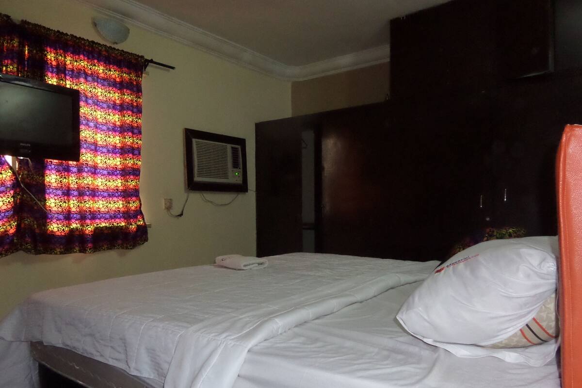 A hotel room with a bed, a television mounted on the wall, and a window with curtains.