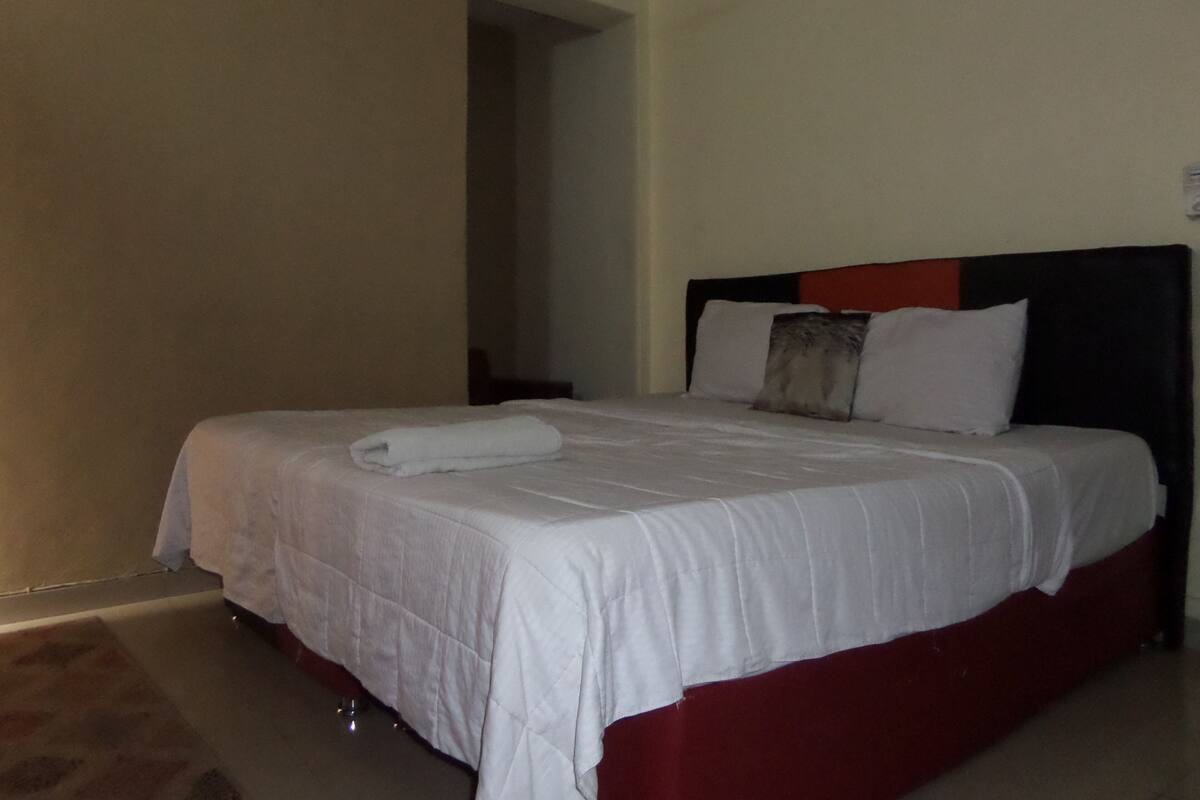 A neatly made bed with a white duvet and a red accent, a pillow, and a folded towel on the side.