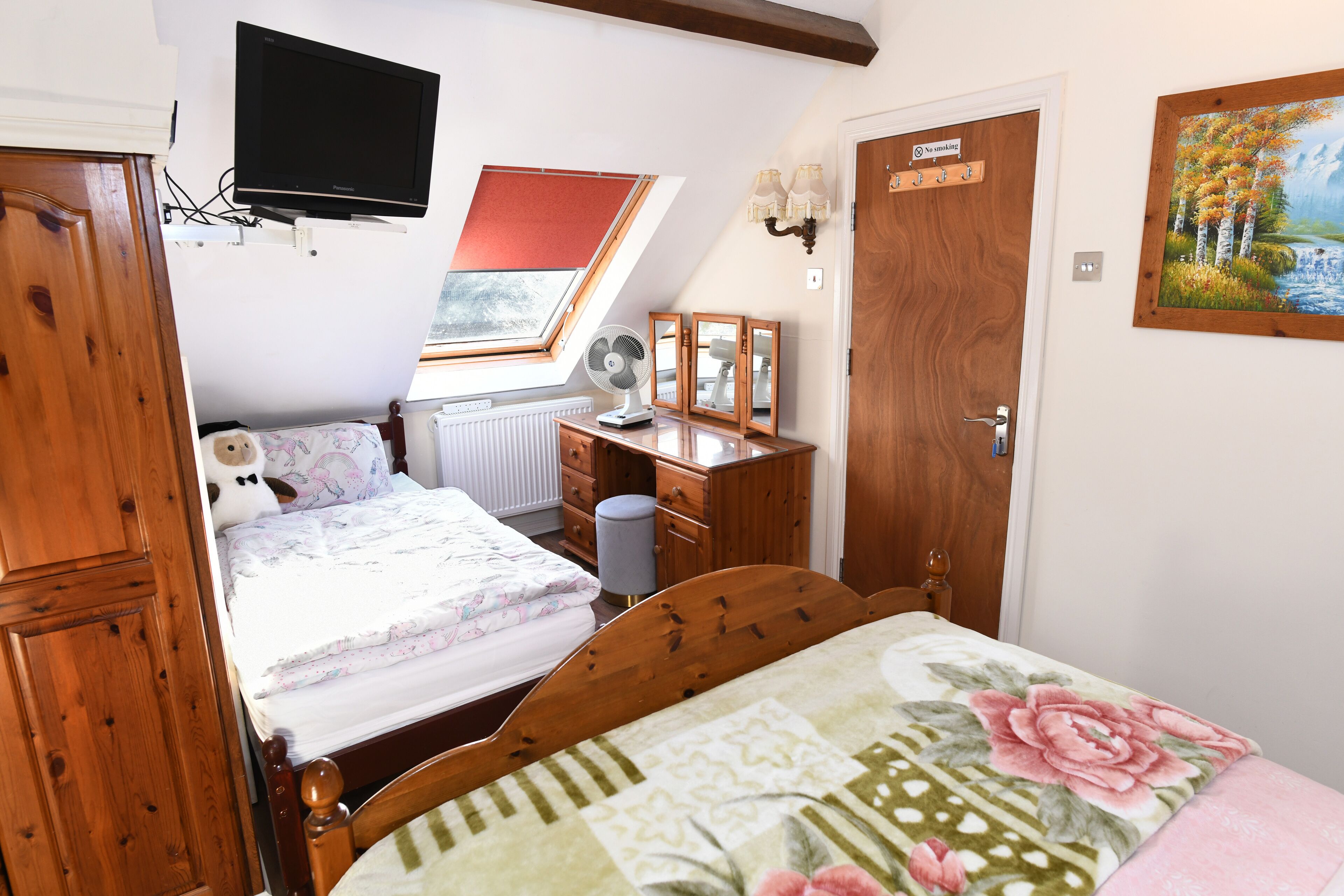 A bedroom with a bed, a desk, a chair, a TV mounted on the wall, a window, and a door.