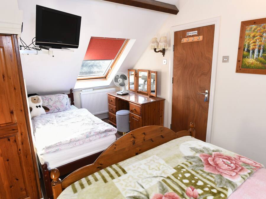 A bedroom with a bed, a desk, a chair, a TV mounted on the wall, a window, and a door.