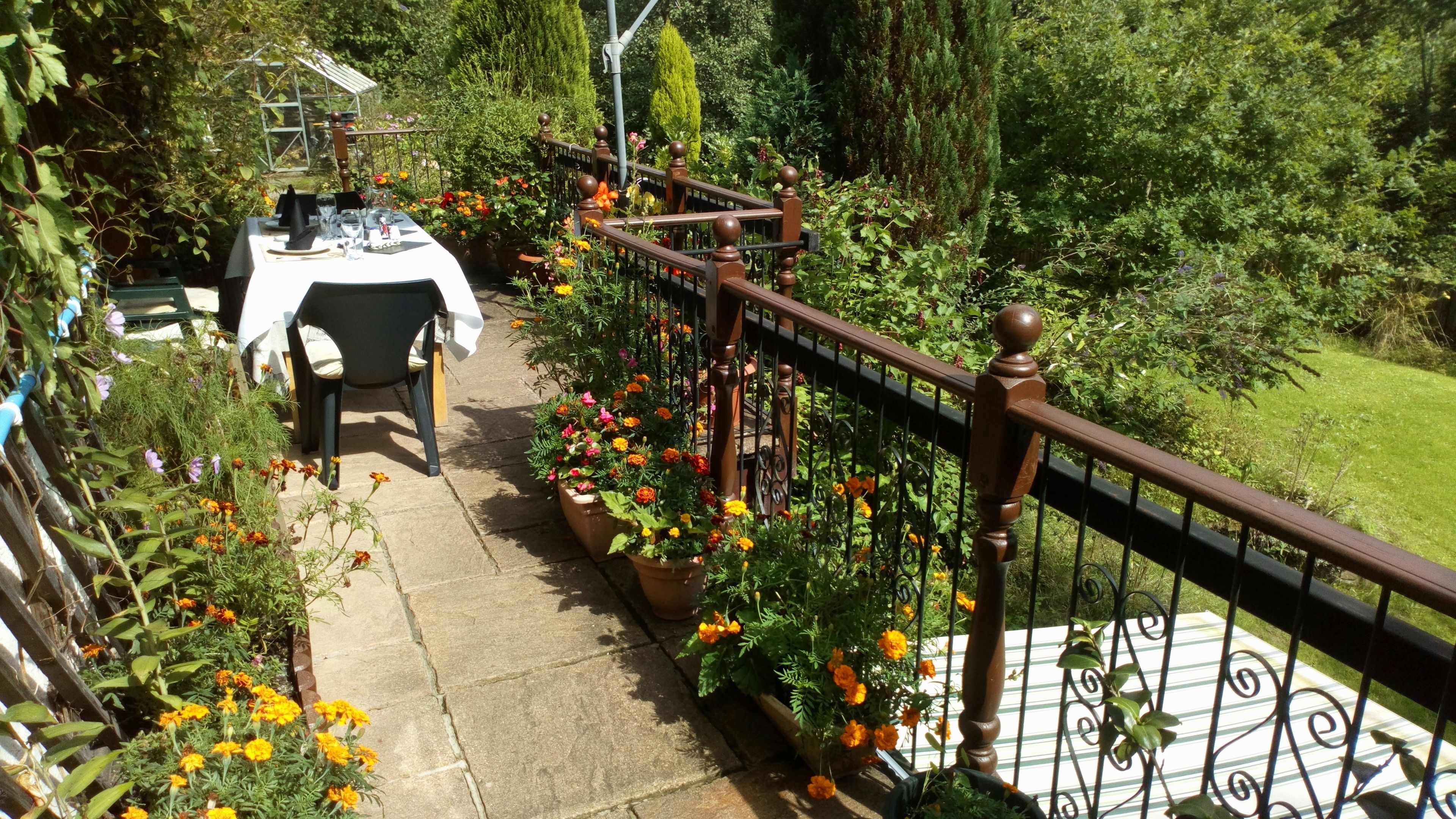 A balcony with a table and chairs, surrounded by potted plants and flowers.