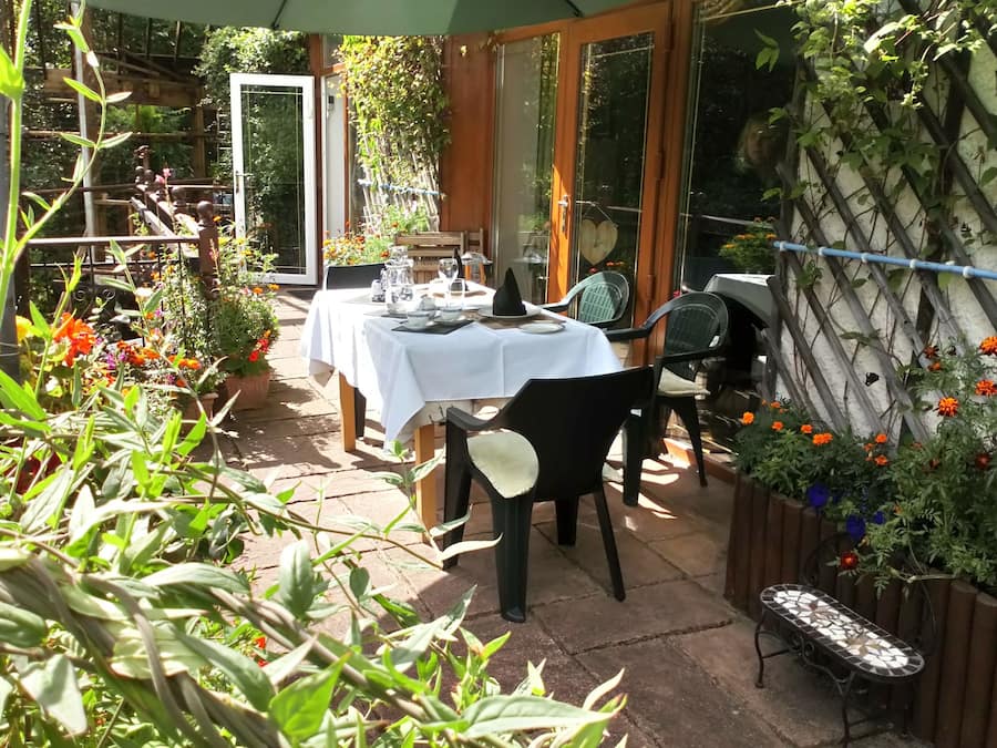 An outdoor dining area with a table set for two, surrounded by potted plants and flowers.