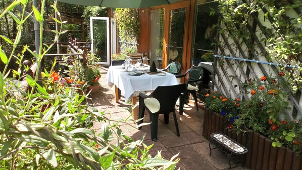 An outdoor dining area with a table set for two, surrounded by potted plants and flowers. - Cilbrwyn Countryside Retreat (Swansea)