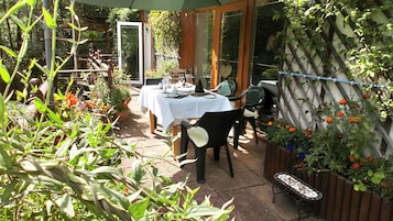 Un área de comedor al aire libre con una mesa dispuesta para dos personas, rodeada de plantas y flores en macetas.