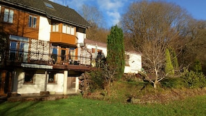 A two-story house with a balcony, a small garden, and a tree in the background. - Cilbrwyn Countryside Retreat (Swansea)