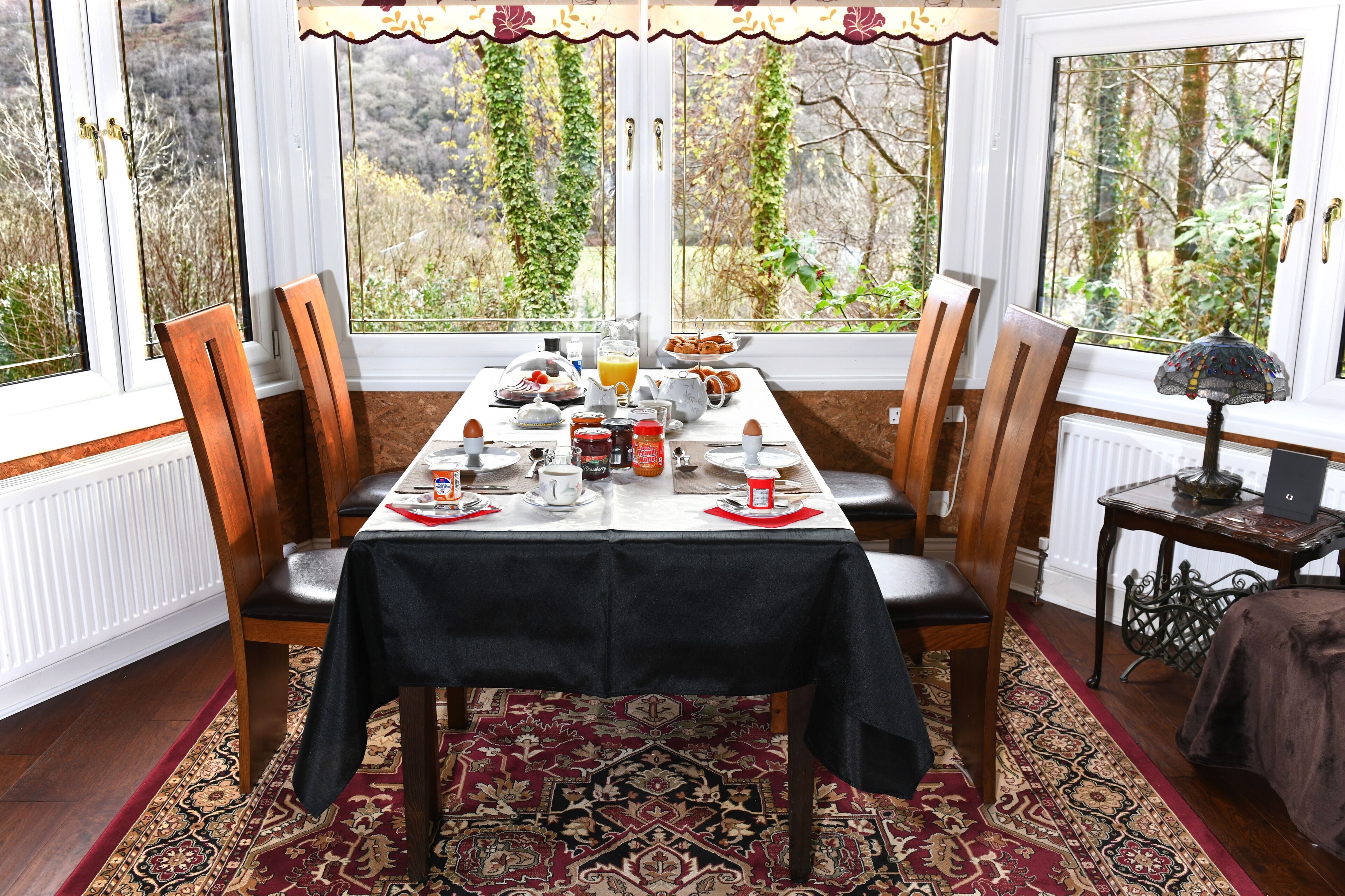 Comedor con mesa dispuesta para cuatro personas, sillas alrededor y vistas a zonas verdes a través de amplios ventanales.