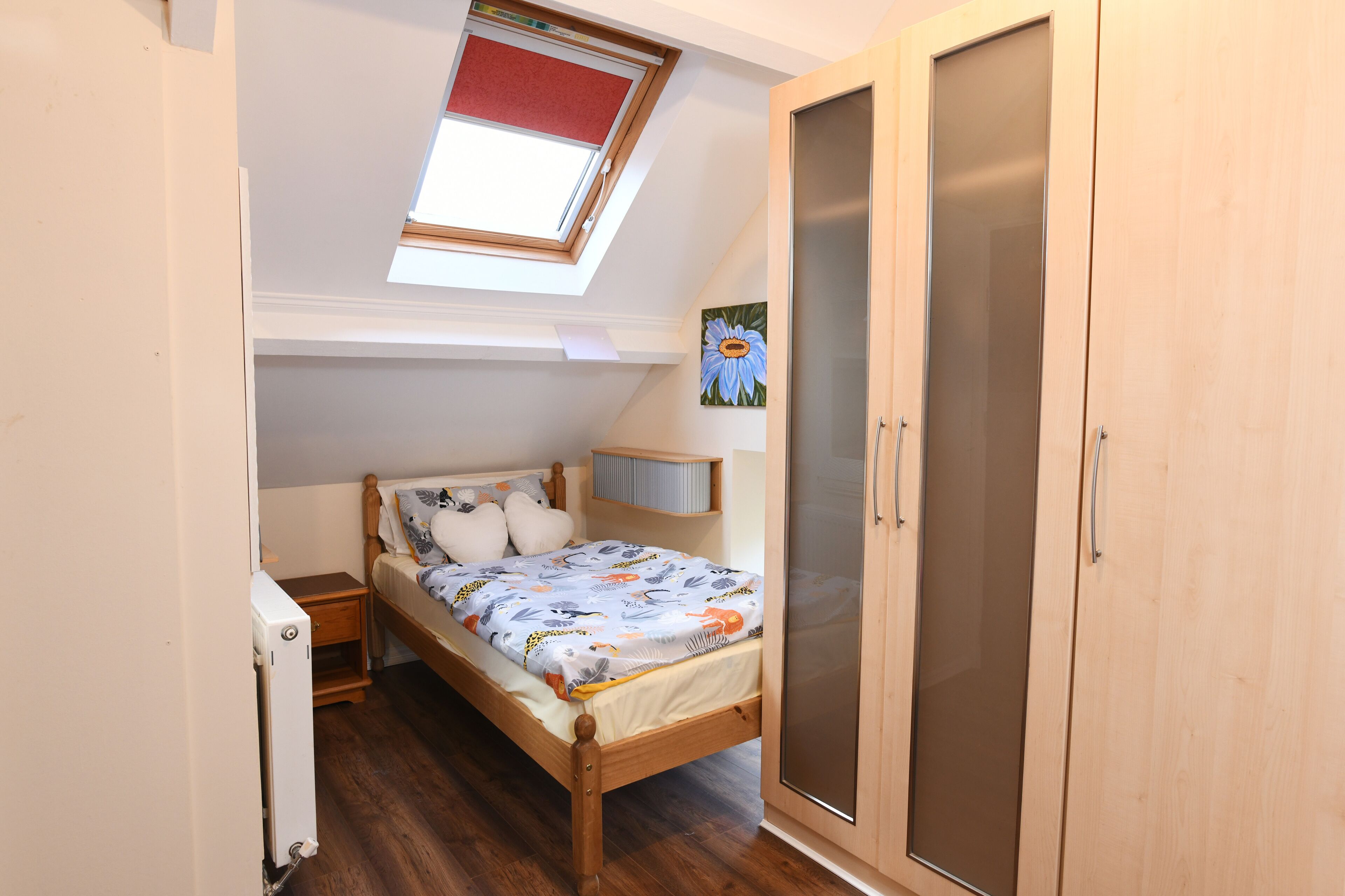 Un dormitorio con tragaluz, una cama con colcha estampada, un armario de madera y una mesita de noche.