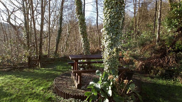 A picnic table surrounded by a circular stone border in a forested area. - Cilbrwyn Countryside Retreat (Swansea)