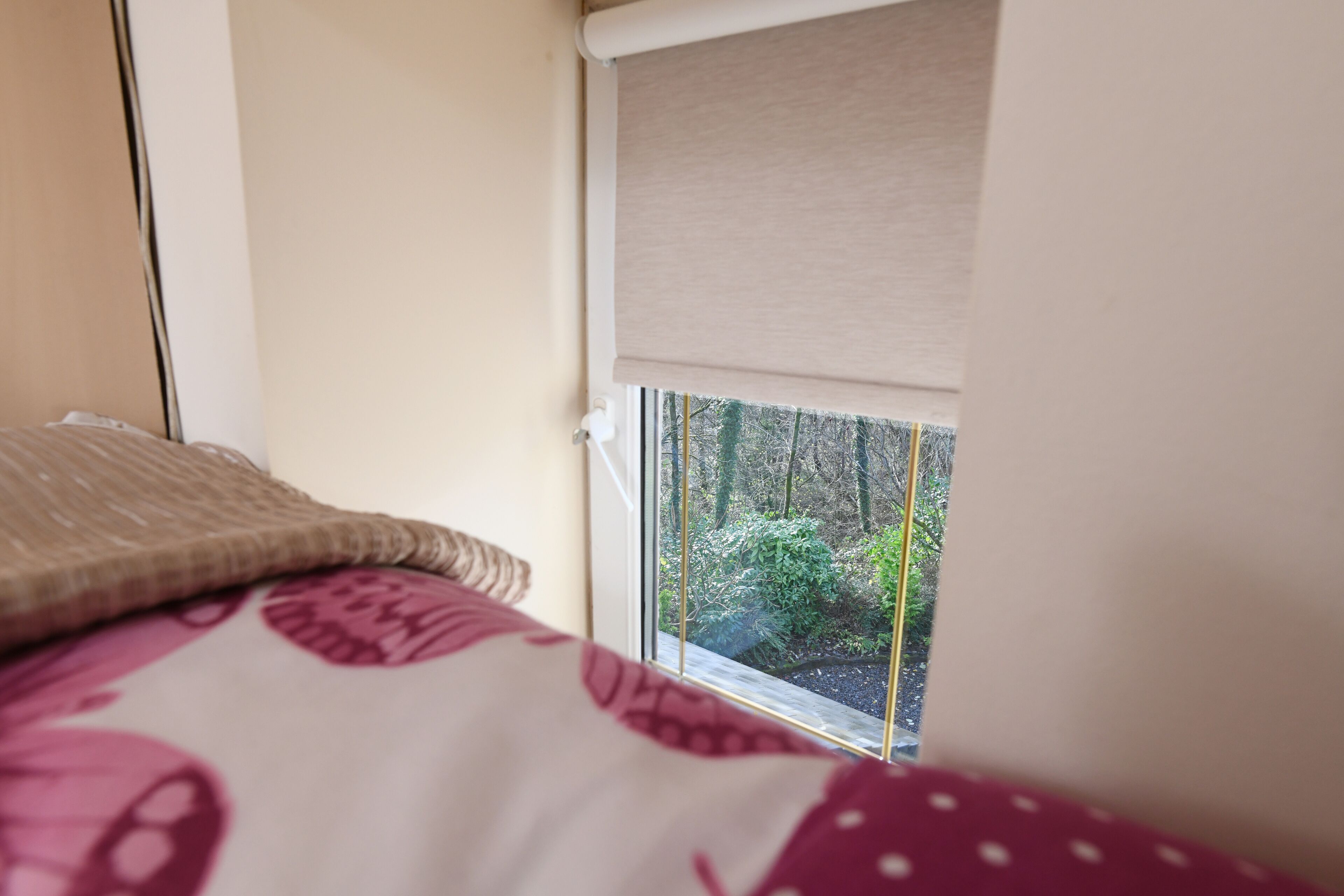 Une chambre avec une fenêtre, un lit recouvert d’une couvre-lit à motifs et une vue sur les arbres à l’extérieur.