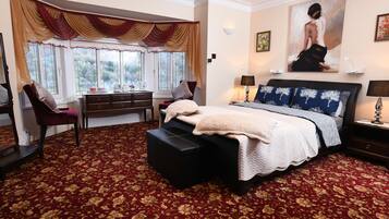 Un dormitorio con una cama grande, un escritorio y una silla. Hay una ventana con cortinas, un cuadro en la pared y suelo alfombrado.