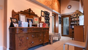 A wooden cabinet with framed photos and certificates, a lace tablecloth-covered table, and a white chair in a room with wooden walls and a tiled floor. - Cilbrwyn Countryside Retreat (Swansea)