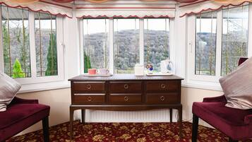 A room with a large bay window, a wooden dresser, two red armchairs, and a patterned carpet.