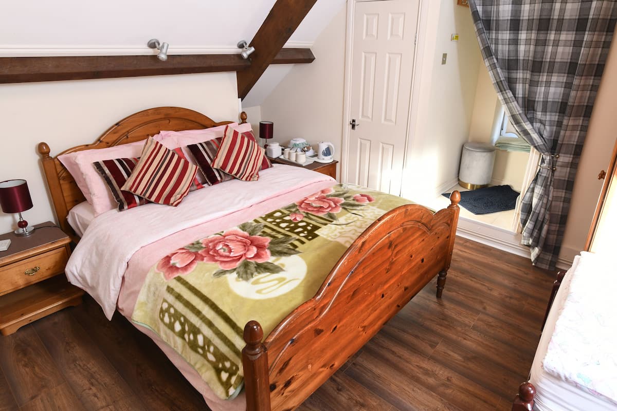Une chambre à coucher avec un lit en bois, une literie à motifs floraux, une table de chevet avec une lampe et une porte avec un rideau.