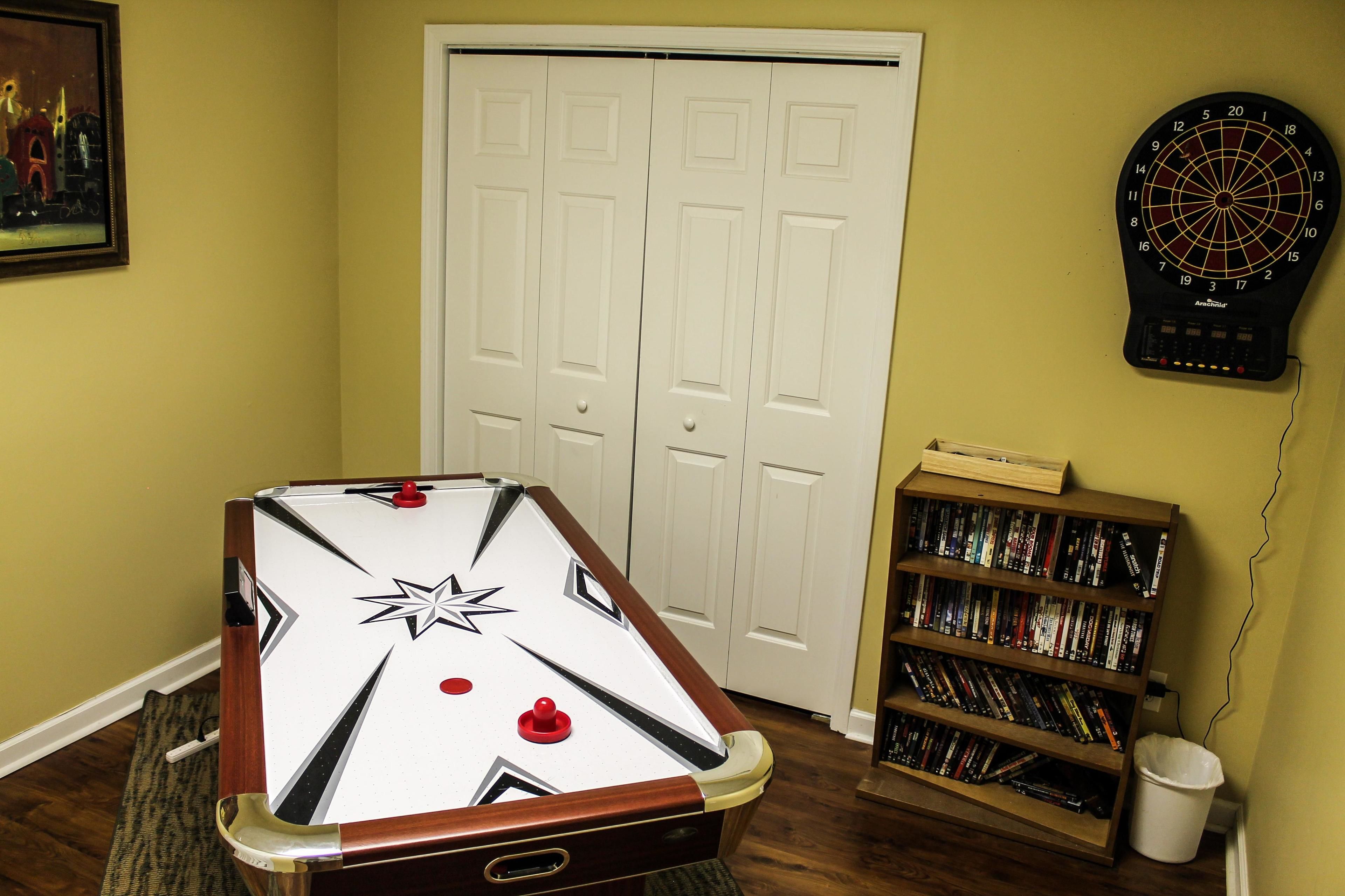 A room with a foosball table, a dartboard, and a bookshelf.
