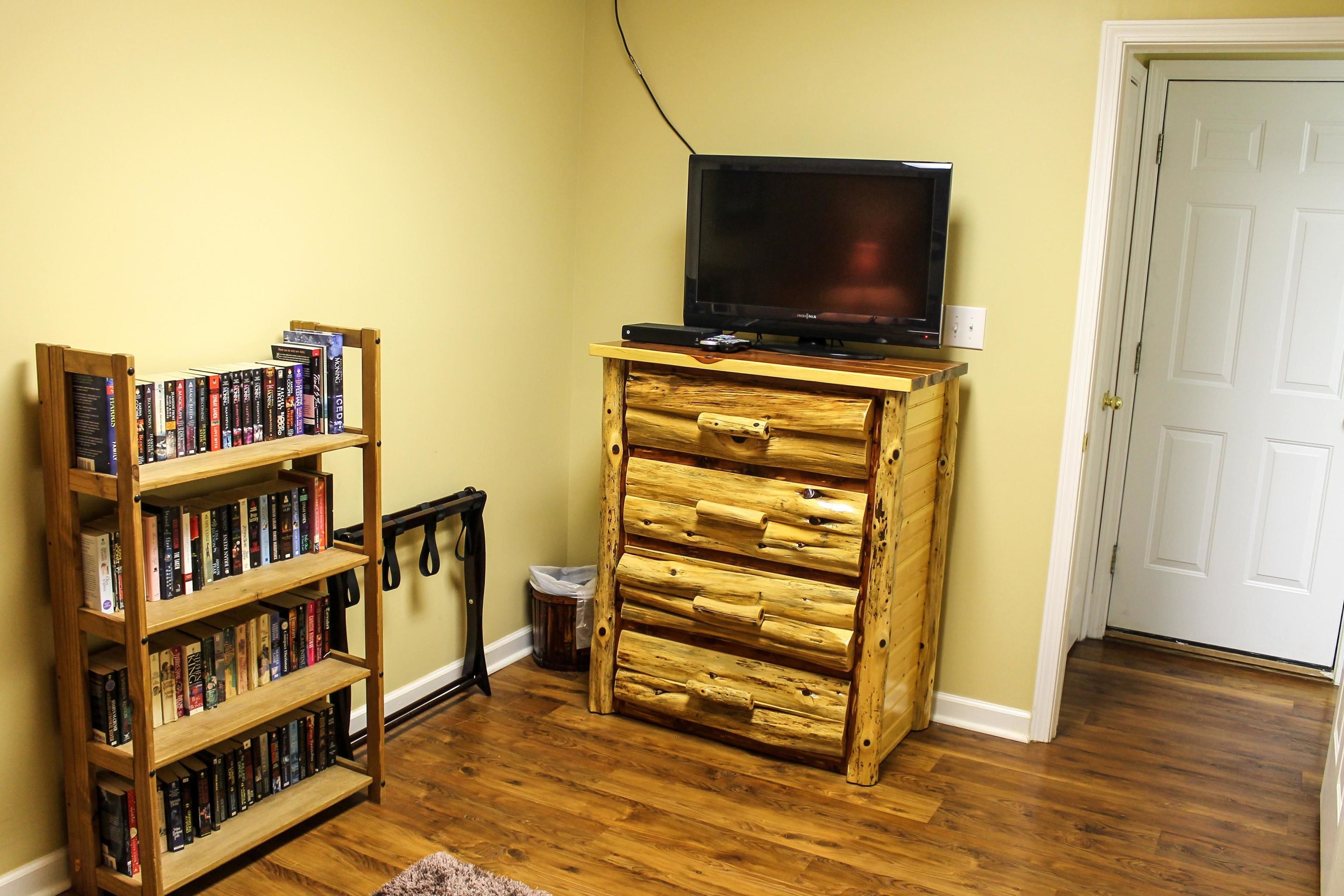 A room with a wooden bookshelf, a wooden chest of drawers, and a television on a wooden stand.