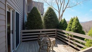 Een houten terras met een leuning, een rieten stoel en een kleine tafel.