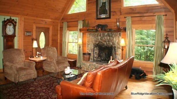 A cozy log cabin interior with a fireplace, leather sofa, and wooden walls. - Lodge at Riversound Apartment (Banner Elk)