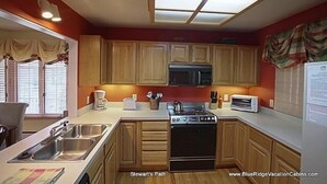 A compact kitchen with wooden cabinets, a microwave, a stove, and a toaster. - Stewart's Path Apartment (Boone)