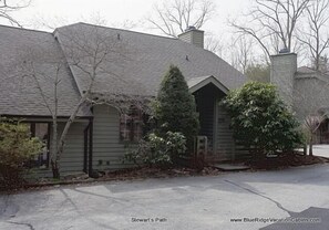 A two-story house with a gabled roof and a chimney. There is a driveway leading to the front door. - Stewart's Path Apartment (Boone)