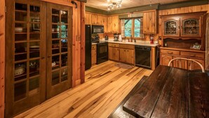 A wooden cabin-style kitchen with a dining table, wooden cabinets, and a ceiling fan.