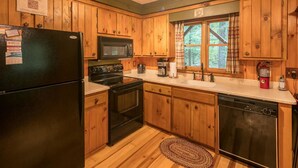 A kitchen with wooden cabinets, a black refrigerator, a microwave, stove, and dishwasher. There is a window with a view of trees.