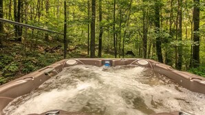 A hot tub in a forested area with a metal railing and a control panel.