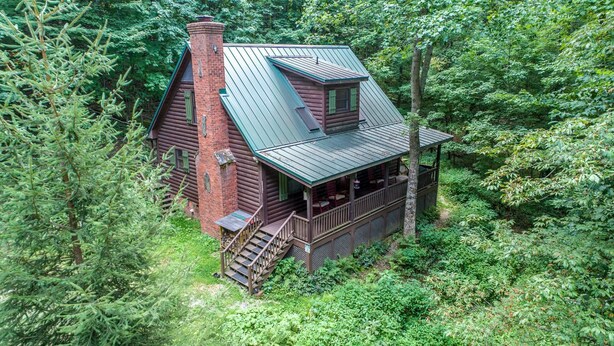 A log cabin with a balcony and a chimney, surrounded by dense forest.