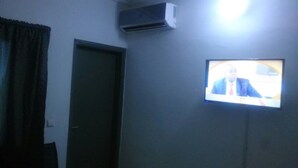 A room with a closed door, an air conditioning unit mounted on the wall, and a television screen displaying a person. - Hotel Les Graces (Abidjan)