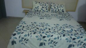 A bed with a floral bedspread and matching pillows in a room with a plain wall and a wooden headboard. - Hotel Les Graces (Abidjan)