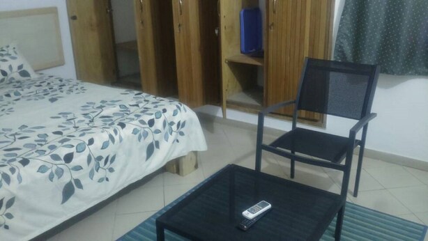 A bedroom with a bed, a chair, a small table, and a wardrobe. - Hotel Les Graces (Abidjan)