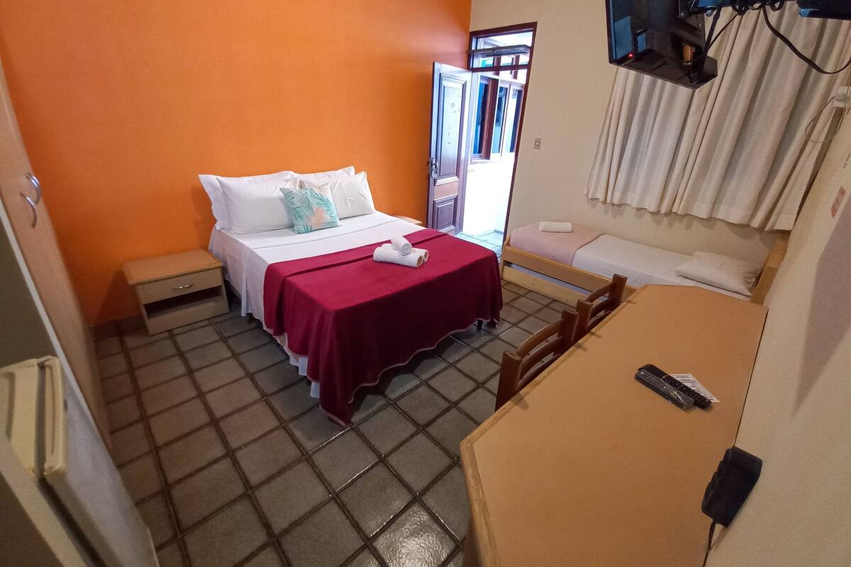 A hotel room with a bed, a small table, a TV, and a window with curtains.
