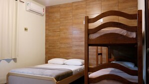 Une chambre avec un lit superposé doté d’une tête de lit en bois, un lit simple avec un matelas gris et un climatiseur fixé au mur.
