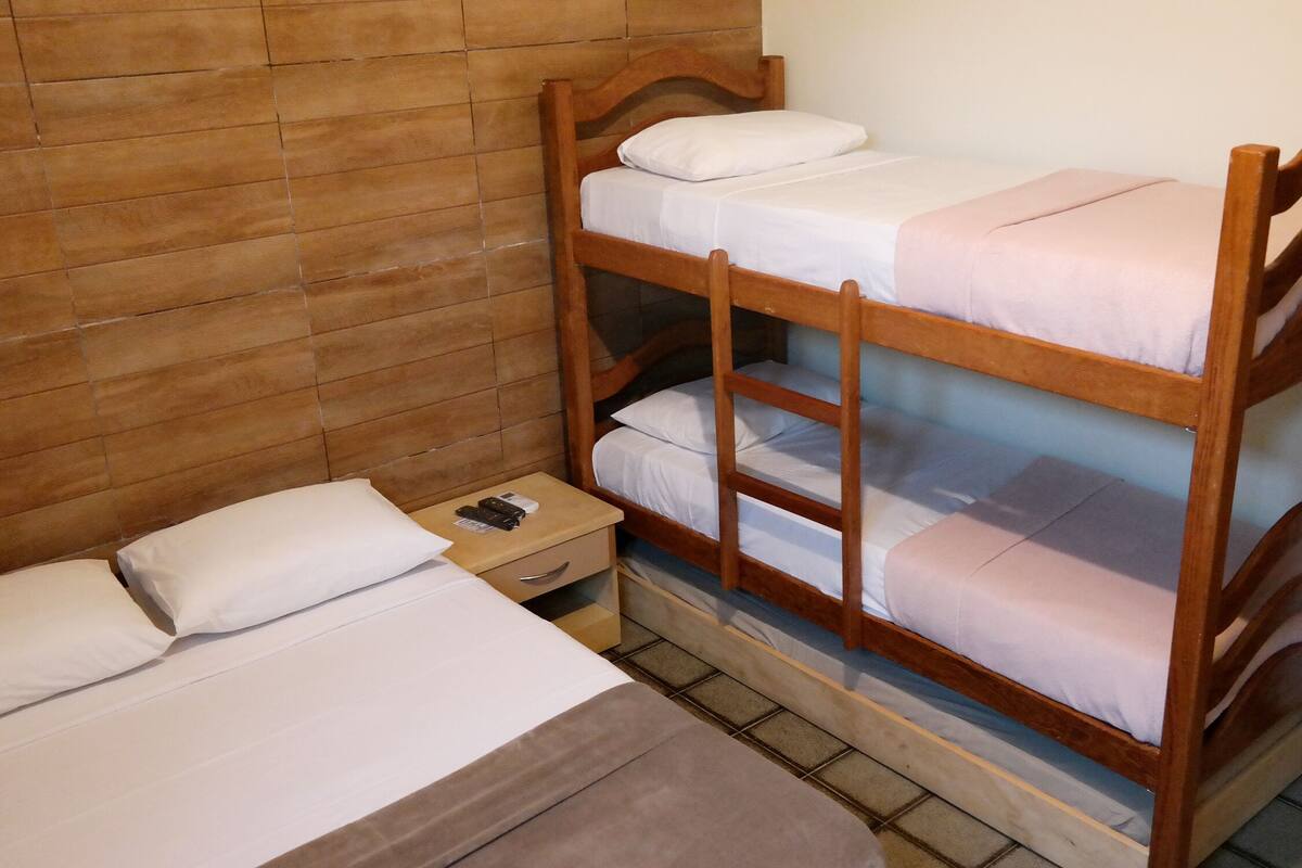 A bunk bed room with a wooden headboard, a bedside table with a remote control, and a single bed with a pillow.