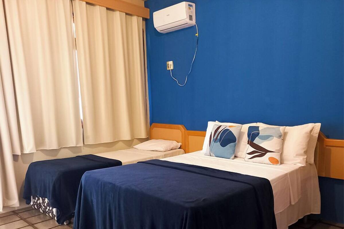 A hotel room with two beds, a blue wall, and an air conditioning unit.