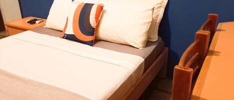 Un letto con una coperta beige, due cuscini e una testiera in legno.