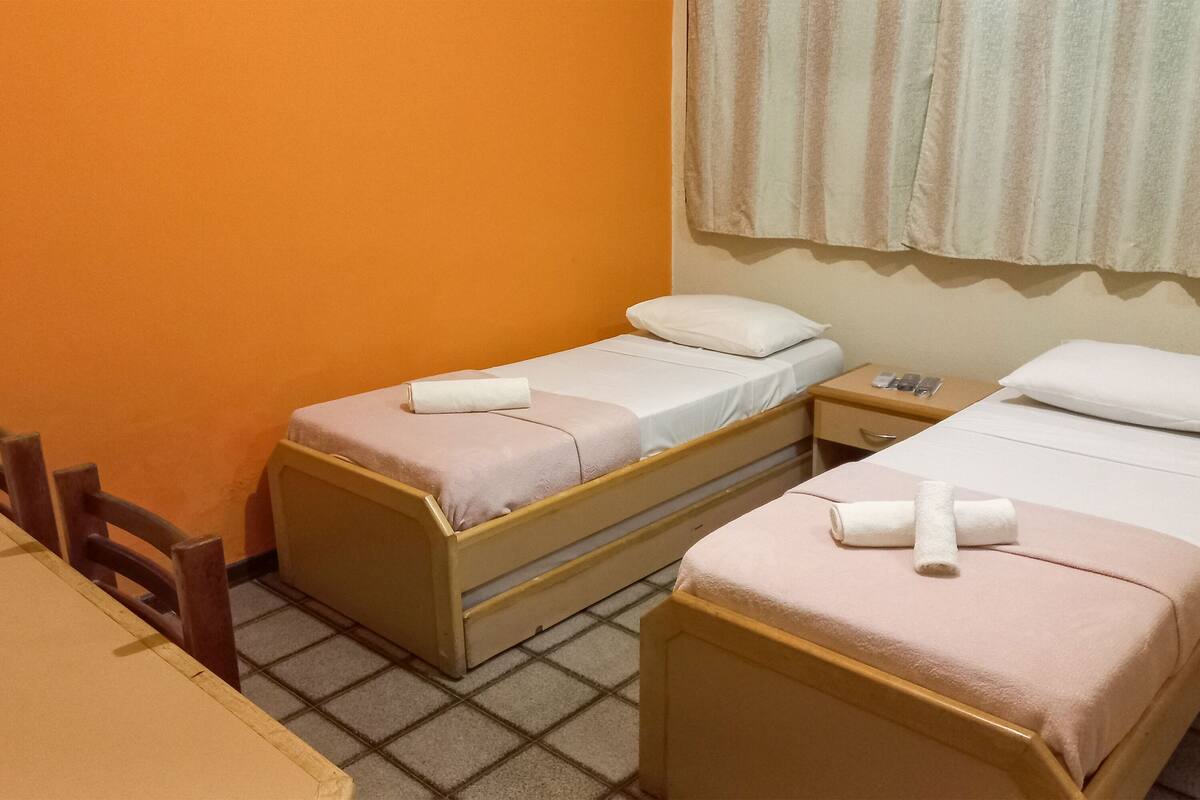 A small hotel room with two single beds, a wooden table, and a window with curtains.