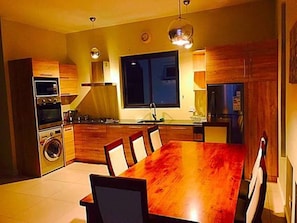 Une cuisine moderne avec des meubles en bois, une grande table à manger et des appareils électroménagers intégrés.