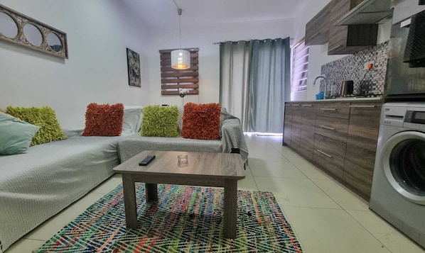 A compact living space with a sofa, a coffee table, a washing machine, and a kitchen area. - Sugareef West Coast (Flic-en-Flac)