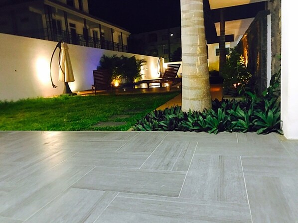 A well-lit outdoor area with a tiled floor, a palm tree, and a seating area with a lamp. - Sugareef West Coast (Flic-en-Flac)