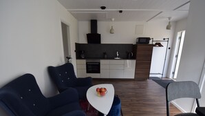 A modern living room with dark blue chairs, a white coffee table with fruit, and a kitchen in the background. - Vänern Property apartments (Grums)