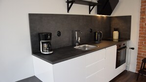A compact kitchen with a black countertop, white cabinets, a stainless steel sink, a coffee maker, a kettle, and a small oven. - Vänern Property apartments (Grums)