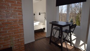 A room with a brick wall, a bed with a white headboard, a desk with a chair, and a window with a view of trees. - Vänern Property apartments (Grums)