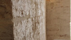 A textured stone wall with a white object on it, a wooden table with a blue and red object, and a white chair. - B&B Piazza Garibaldi (Santeramo in Colle)