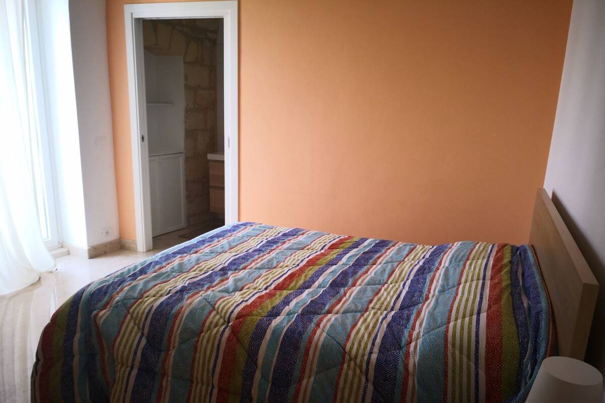 Une chambre à coucher avec un lit, une table de chevet, une porte et une fenêtre avec des rideaux.